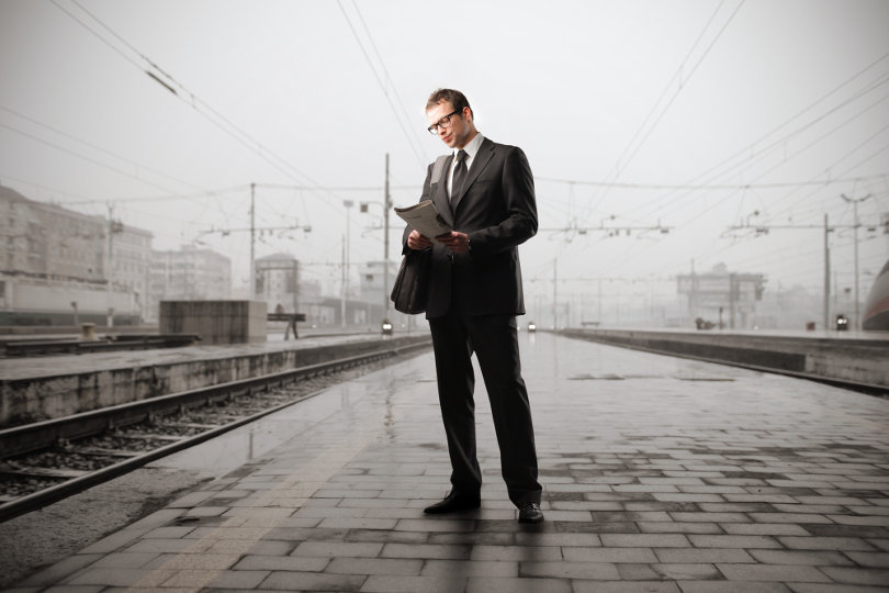 Businessman reading a newspaper standing on the platform of a train station